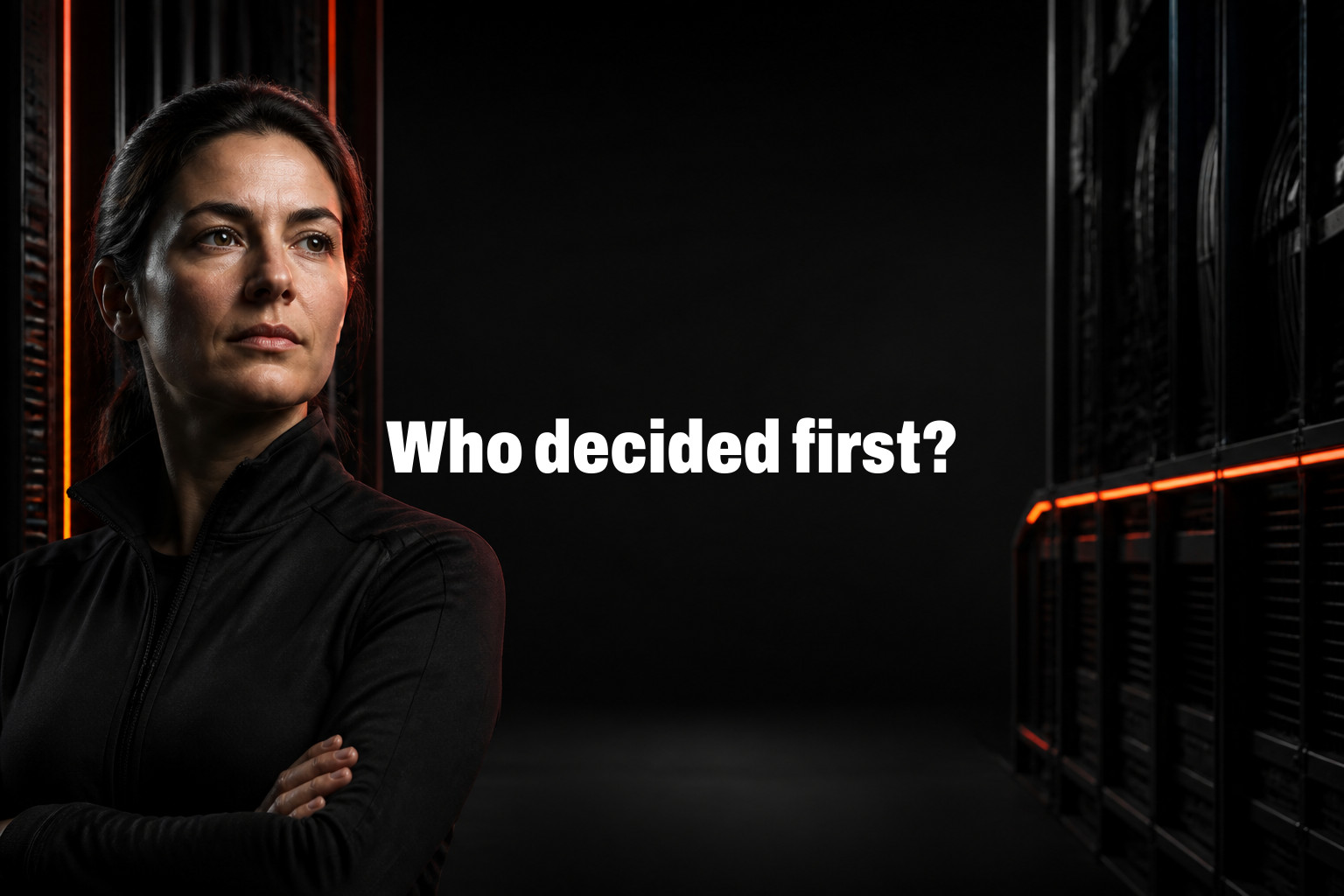 Who decided first? Woman with folded arms stands in a dark server room beside black server racks lit with red lights.